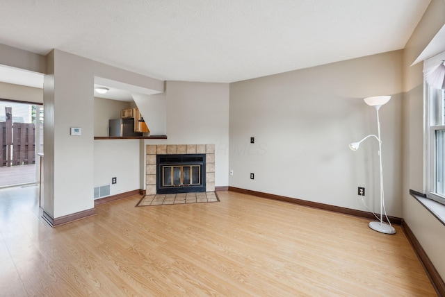 unfurnished living room with wood finished floors, a tiled fireplace, and baseboards