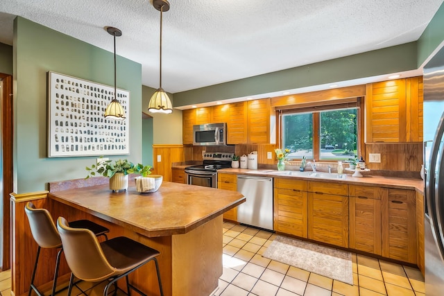 12502 Barbara Dr, Kenton, OH 43326 - kitchen featuring appliances with stainless steel finishes, a sink, a textured ceiling, a kitchen breakfast bar, and decorative light fixtures