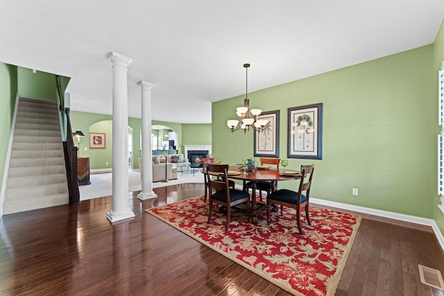 dining room with dark wood-type flooring, a glass covered fireplace, decorative columns, stairway, and arched walkways