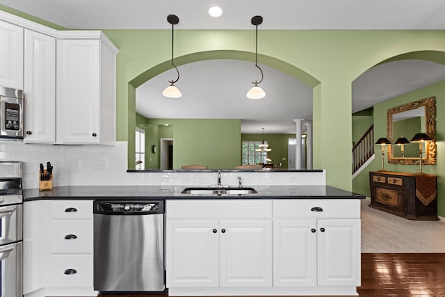 kitchen featuring appliances with stainless steel finishes, a sink, arched walkways, and white cabinetry
