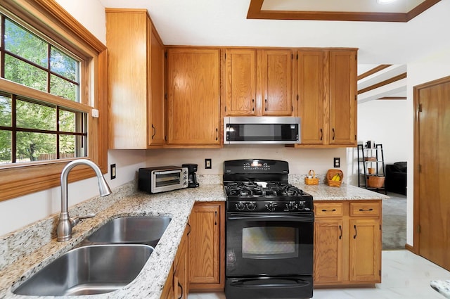 kitchen with stainless steel microwave, gas stove, a sink, light stone countertops, and brown cabinets