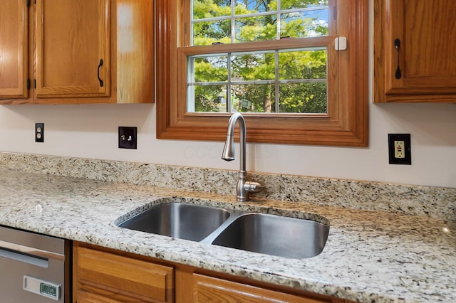 kitchen with a sink, brown cabinetry, light stone countertops, and stainless steel dishwasher