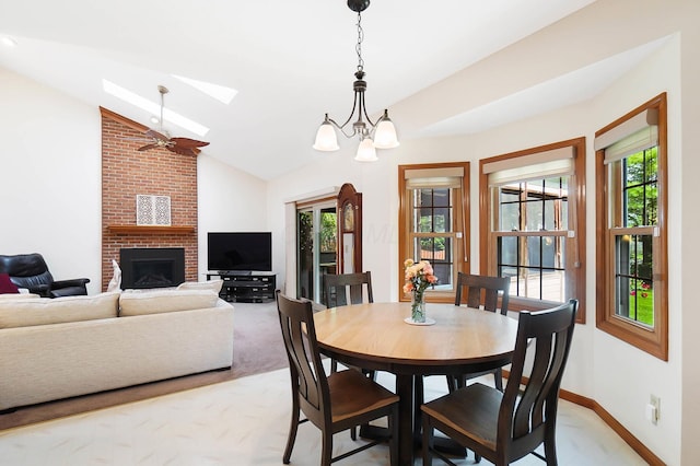dining area with a skylight, lofted ceiling, a fireplace, baseboards, and ceiling fan