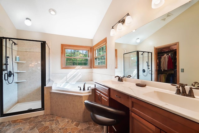 full bathroom with vaulted ceiling, a shower stall, a bath, a walk in closet, and double vanity