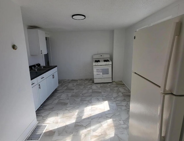 kitchen with white appliances, a sink, dark countertops, light marble finish flooring, and white cabinetry