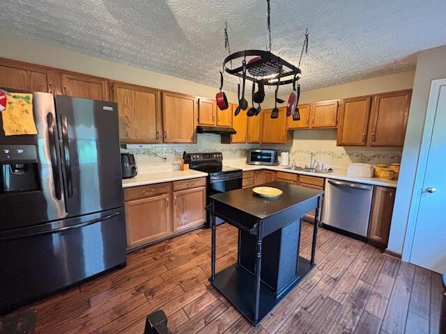 kitchen featuring appliances with stainless steel finishes, under cabinet range hood, a sink, a textured ceiling, and dark wood-style floors