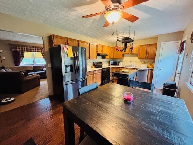 kitchen with refrigerator with ice dispenser, black range with electric stovetop, under cabinet range hood, light countertops, and dark wood-style floors
