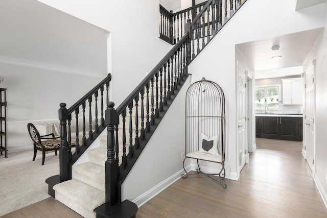 stairway with wood finished floors, baseboards, and ornamental molding
