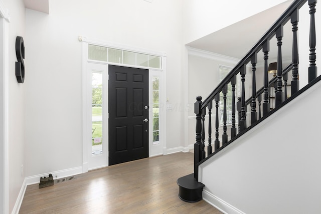 foyer entrance with baseboards, wood finished floors, stairs, ornamental molding, and a high ceiling