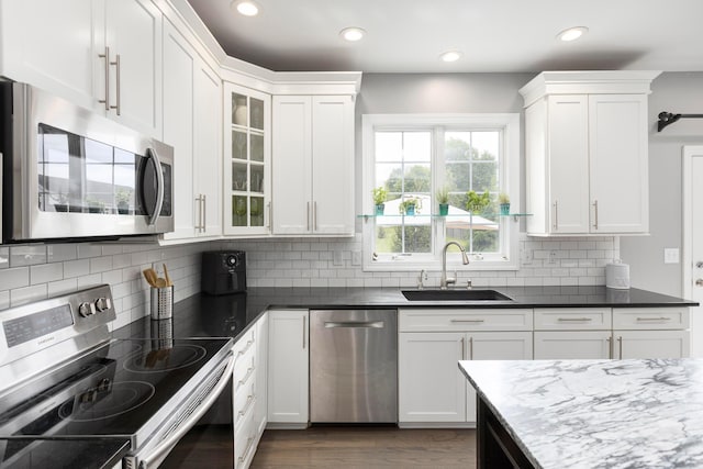 kitchen featuring appliances with stainless steel finishes, a sink, white cabinets, recessed lighting, and glass insert cabinets