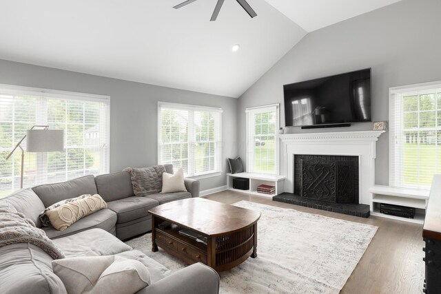 living room featuring a fireplace with raised hearth, a ceiling fan, plenty of natural light, lofted ceiling, and wood finished floors