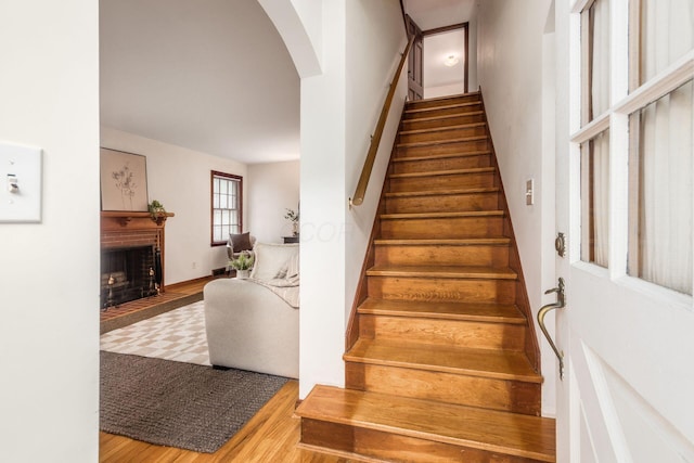 stairs featuring arched walkways, wood finished floors, and a brick fireplace