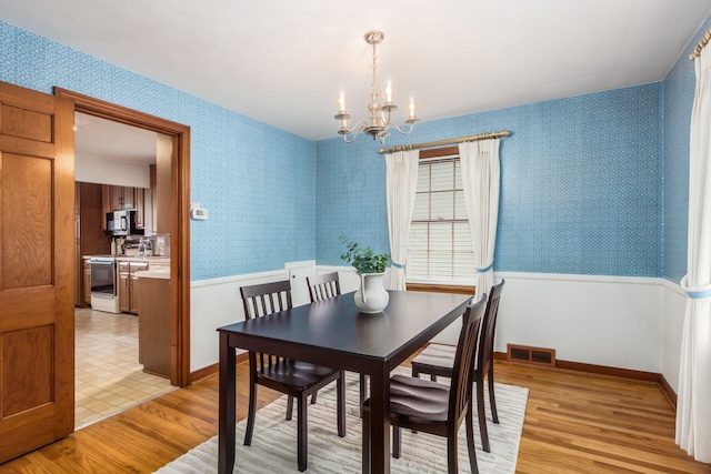 dining space featuring wallpapered walls, a chandelier, light wood-style flooring, and a wainscoted wall