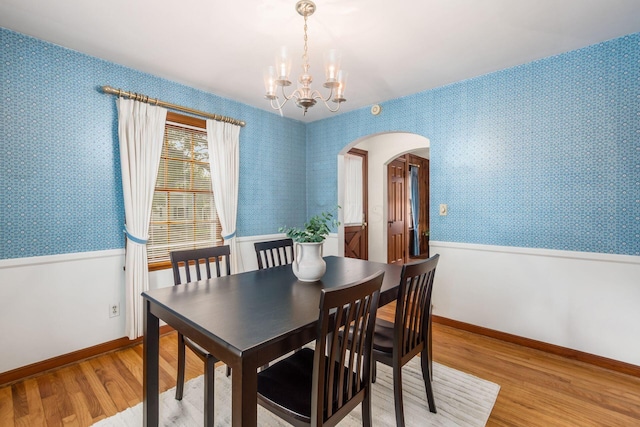 dining area featuring arched walkways, light wood-style flooring, a chandelier, wallpapered walls, and baseboards