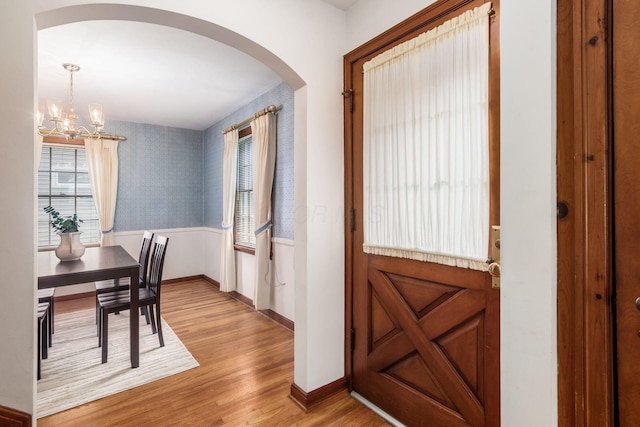 foyer entrance with wallpapered walls, arched walkways, a chandelier, light wood finished floors, and plenty of natural light