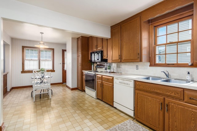 kitchen featuring white appliances, brown cabinets, a sink, baseboards, and light countertops