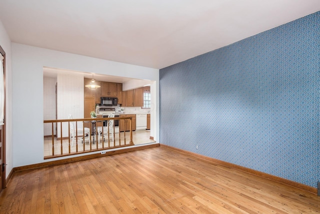 unfurnished living room with wallpapered walls, light wood-type flooring, baseboards, and an accent wall