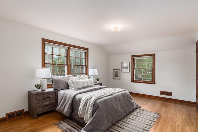 bedroom with lofted ceiling, light wood-style floors, multiple windows, and baseboards