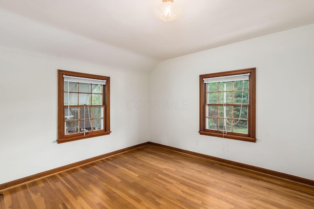 unfurnished room featuring lofted ceiling, baseboards, and wood finished floors