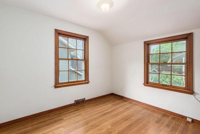 spare room featuring baseboards, lofted ceiling, and light wood-type flooring