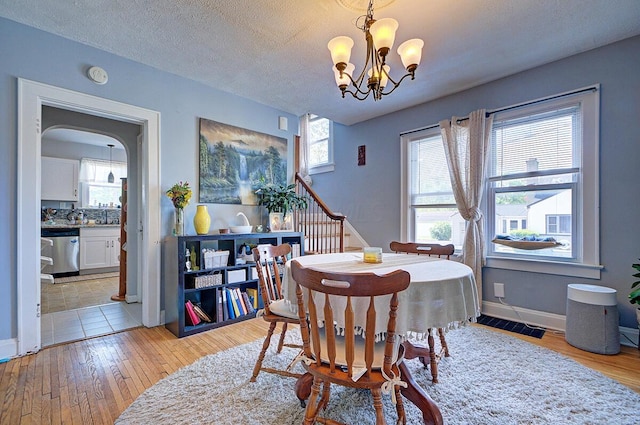 1306-1308 Wilson Ave, Columbus, OH 43206 - dining area featuring light wood-style flooring, a chandelier, baseboards, arched walkways, and stairs