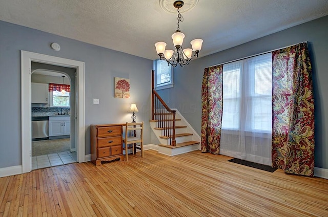 1306-1308 Wilson Ave, Columbus, OH 43206 - dining room featuring light wood-type flooring, a chandelier, stairway, baseboards, and a textured ceiling