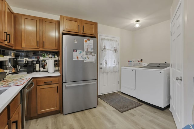 kitchen with appliances with stainless steel finishes, independent washer and dryer, brown cabinetry, light countertops, and light wood-style floors