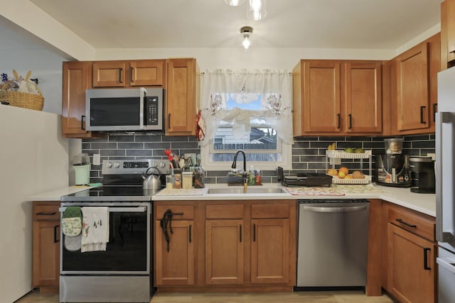 kitchen featuring stainless steel appliances, a sink, decorative backsplash, light countertops, and brown cabinets