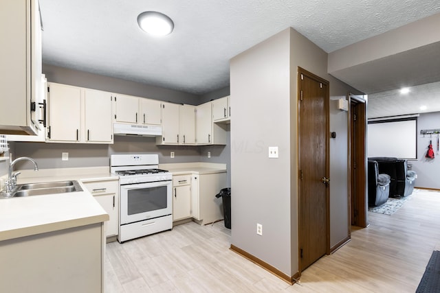 kitchen featuring white range with gas stovetop, a sink, under cabinet range hood, and light wood-type flooring