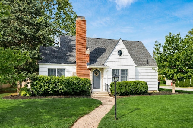 view of front of property featuring a chimney, a front yard, and roof with shingles