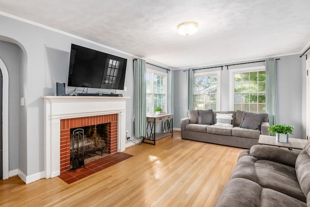 living area featuring arched walkways, wood finished floors, baseboards, ornamental molding, and a fireplace