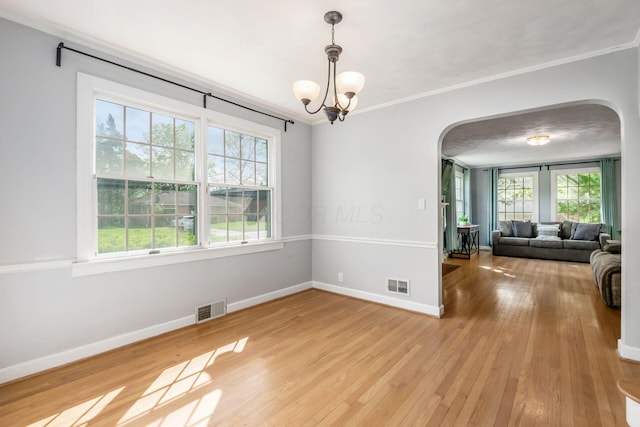 empty room with arched walkways, plenty of natural light, baseboards, and ornamental molding