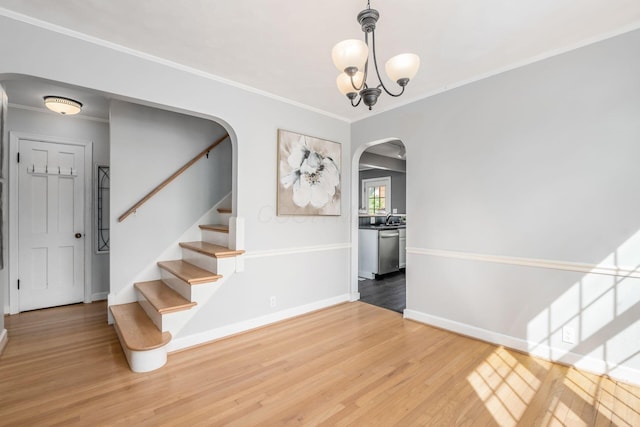 stairway with arched walkways, wood finished floors, baseboards, and crown molding