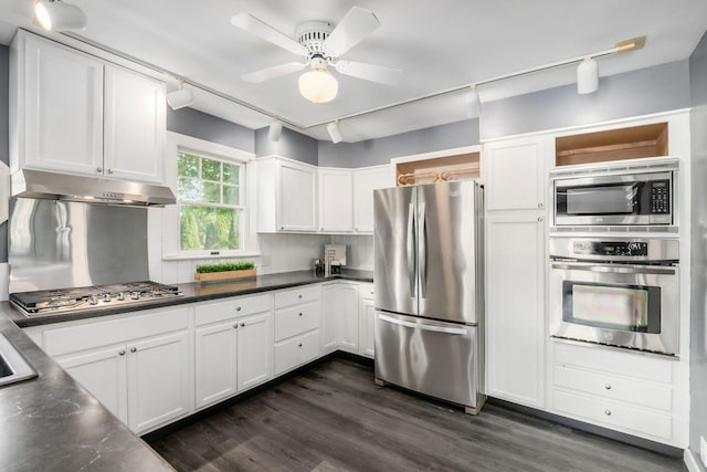 kitchen featuring stainless steel appliances, under cabinet range hood, track lighting, white cabinets, and dark countertops