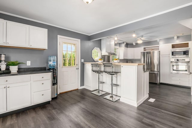 kitchen with appliances with stainless steel finishes, a peninsula, white cabinetry, dark wood-style flooring, and a ceiling fan