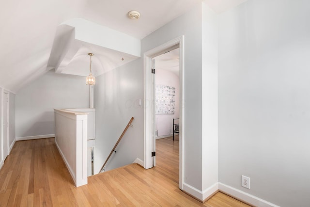 hall with an upstairs landing, light wood-type flooring, baseboards, and lofted ceiling