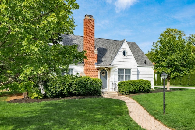 view of front of property featuring a shingled roof, a chimney, and a front lawn