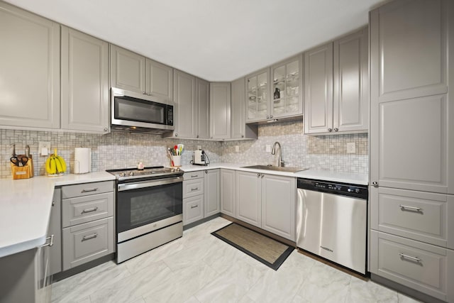 kitchen with stainless steel appliances, a sink, gray cabinetry, light countertops, and backsplash