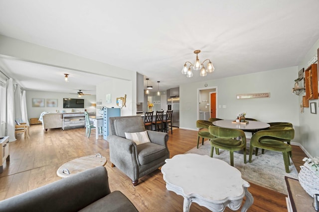 living area featuring a chandelier, wood finished floors, ceiling fan, and baseboards