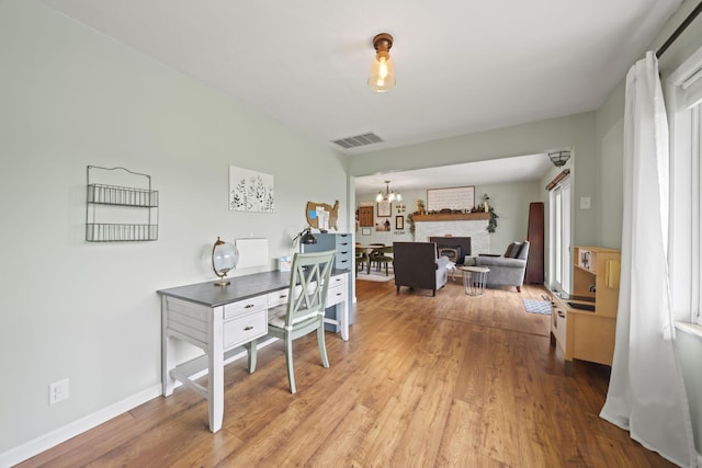 office area featuring light wood-style flooring, a chandelier, a brick fireplace, and baseboards
