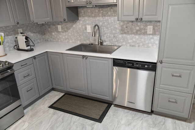 kitchen with stainless steel appliances, gray cabinetry, a sink, backsplash, and light countertops