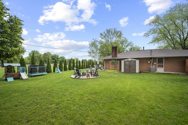view of grassy yard featuring a trampoline, a playground, a storage shed, an outdoor structure, and a patio area