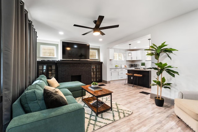 living room with a ceiling fan, light wood finished floors, baseboards, a brick fireplace, and recessed lighting