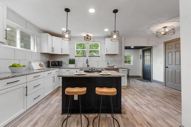 kitchen with tasteful backsplash, white cabinets, light wood finished floors, a kitchen island, and recessed lighting