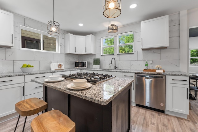 kitchen with stainless steel appliances, a sink, decorative backsplash, light wood-type flooring, and white cabinets