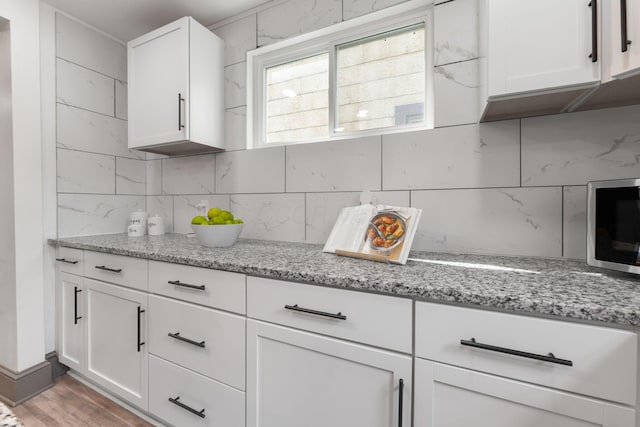 kitchen featuring tasteful backsplash, stainless steel microwave, and white cabinetry