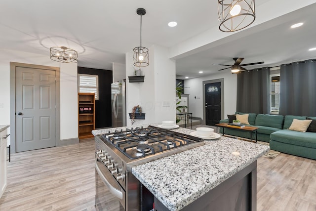 kitchen with appliances with stainless steel finishes, light wood-style floors, light stone counters, pendant lighting, and a ceiling fan