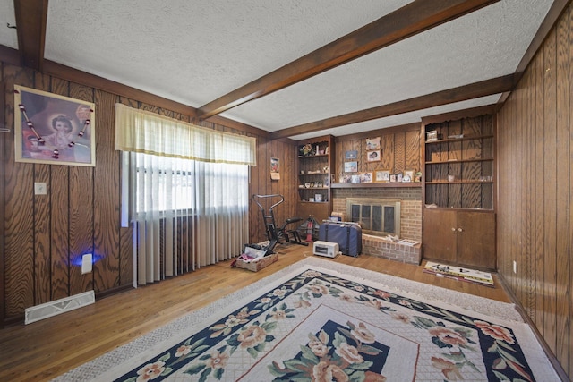 6329 Birkewood St, Columbus, OH 43229 - living room featuring wood walls, wood finished floors, a textured ceiling, beam ceiling, and a brick fireplace
