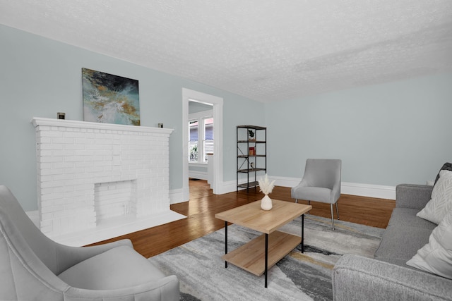 living area with wood finished floors, a textured ceiling, baseboards, and a brick fireplace