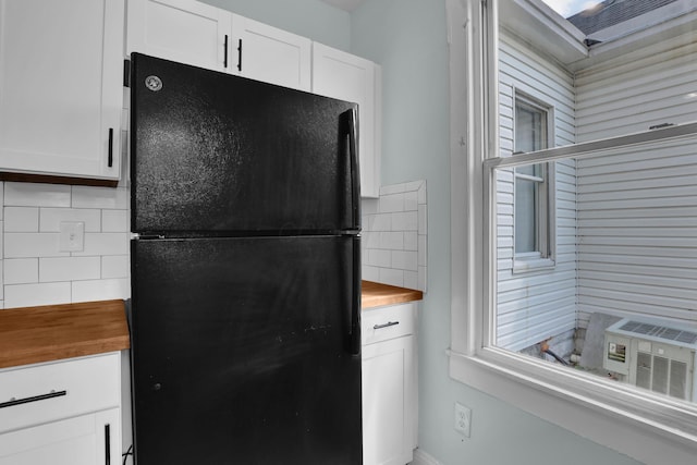 kitchen with freestanding refrigerator, butcher block counters, backsplash, and white cabinetry